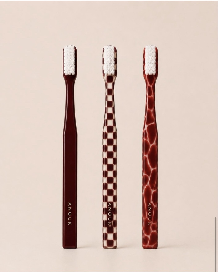 Three Anouk toothbrushes in solid, checkerboard and marbled oxblood finishes